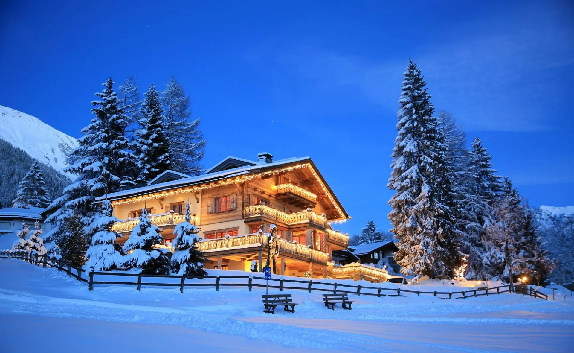 Chalet Kalem in Klosters at dusk, lit up in deep snow among fir trees