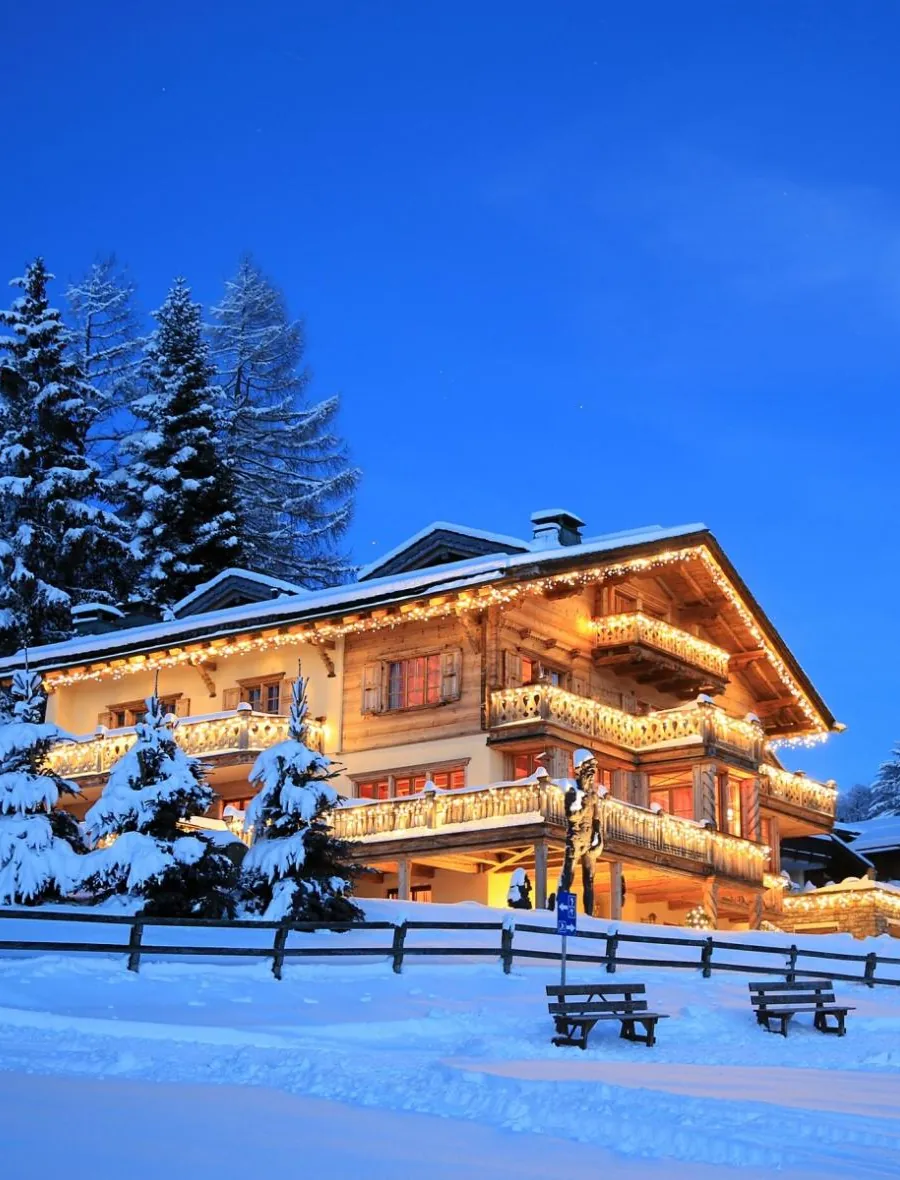 Chalet Kalem in Klosters at dusk, lit up in deep snow among fir trees
