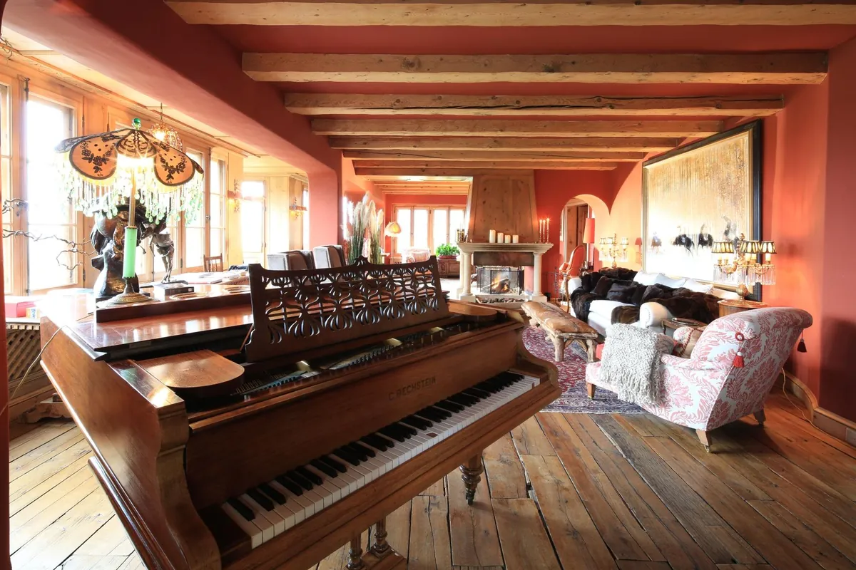 The drawing room at Chalet Kalem, Klosters, with a grand piano, beams and antique rugs