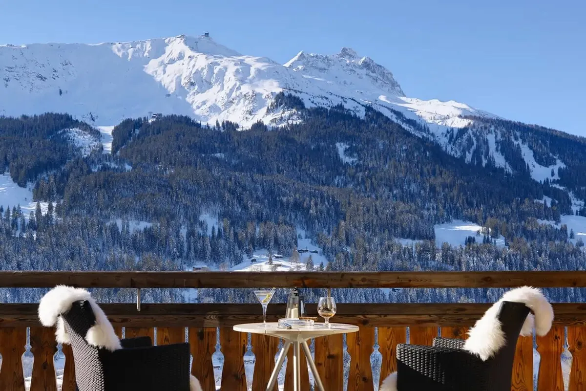 A balcony table with sheepskins and breakfast at Chalet Kolin, Klosters, facing snowy peaks